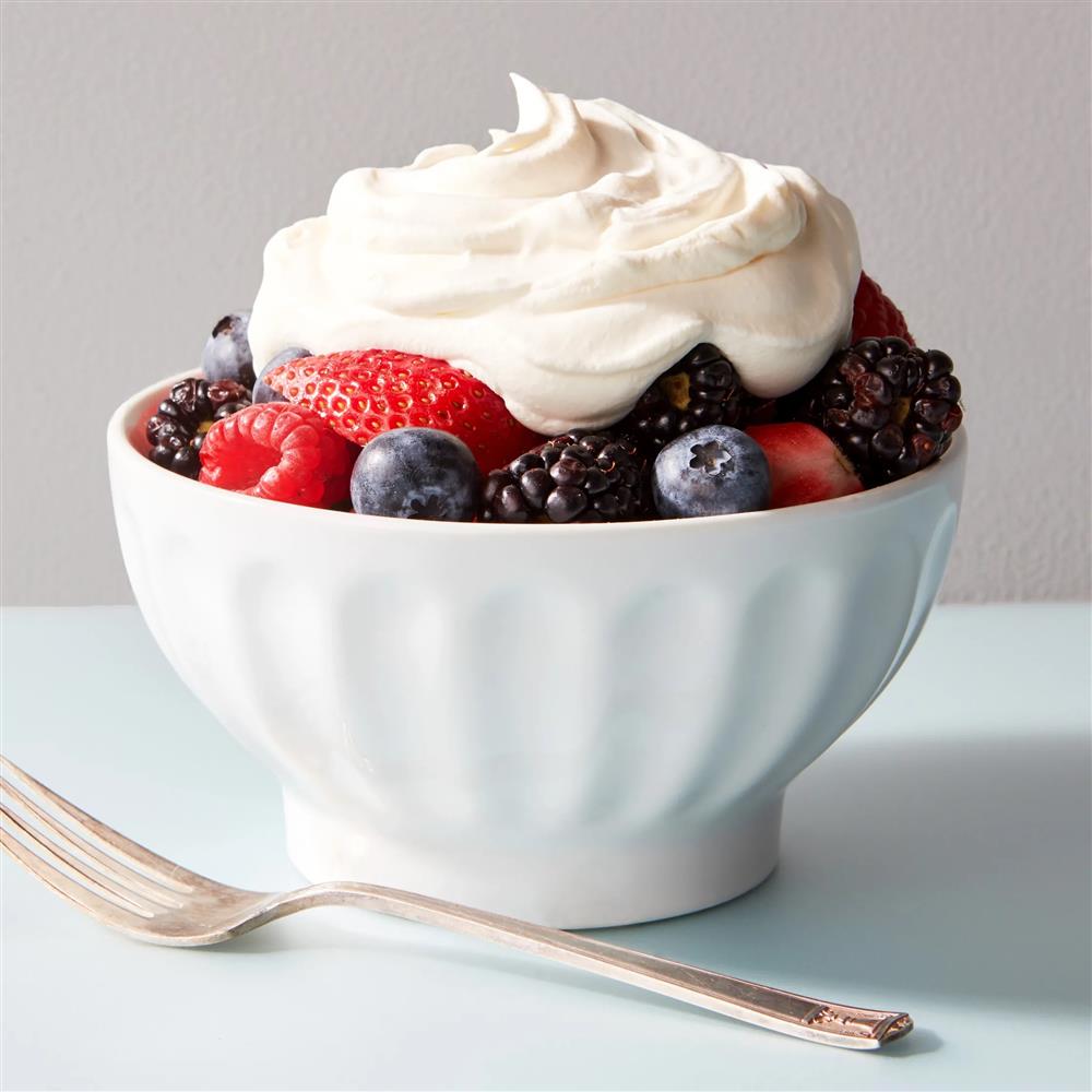 A bowl full of cream and pieces of strawberries, blueberries and blackberries